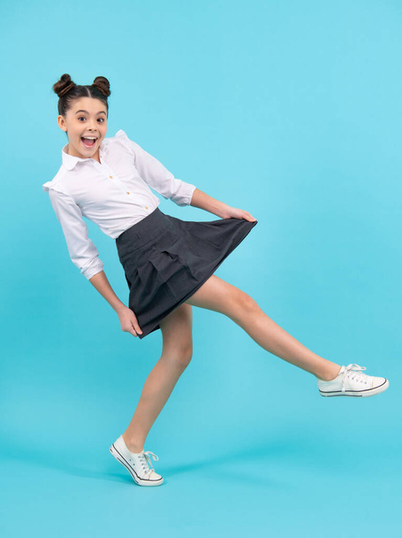 Full length jump of teenager girl on blue isolated studio wear casual skirt and shirt. Funny school girl, amazed kid genius, excited young student - Valokuva, kuva