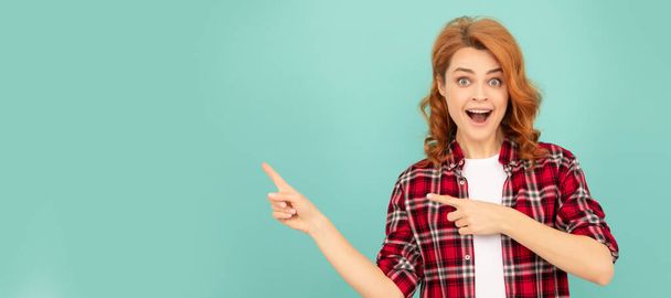 amazed redhead woman in checkered shirt point finger on blue background. Woman isolated face portrait, banner with mock up copyspace - Photo, Image