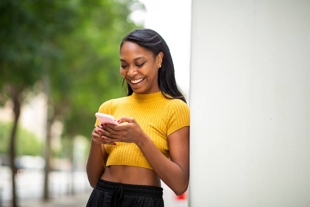 Ευτυχισμένη μαύρη γυναίκα μηνυμάτων χρησιμοποιώντας το κινητό τηλέφωνο σε εξωτερικούς χώρους στην πόλη - Φωτογραφία, εικόνα