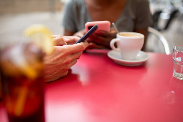 Руки черной женщины и кавказского мужчины с помощью мобильного телефона в кафе на открытом воздухе - Фото, изображение