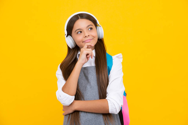 School girl, teenager student in headphones on yellow isolated studio background. School and music education concept. Back to school. Thinking face, thoughtful emotions of teenager girl - 写真・画像
