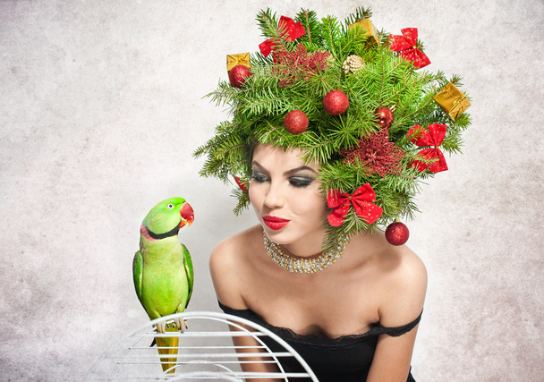 Beautiful creative Xmas makeup and hair style indoor shot. Beauty Fashion Model Girl. Winter. Beautiful attractive girl with Christmas tree accessories in studio speaking with a green parrot. - Fotoğraf, Görsel
