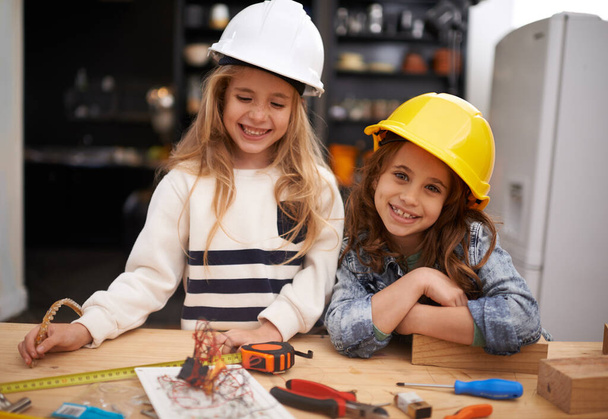 Pequeños inventores en ciernes. dos niñas en sombreros duros jugando con herramientas en casa - Foto, imagen