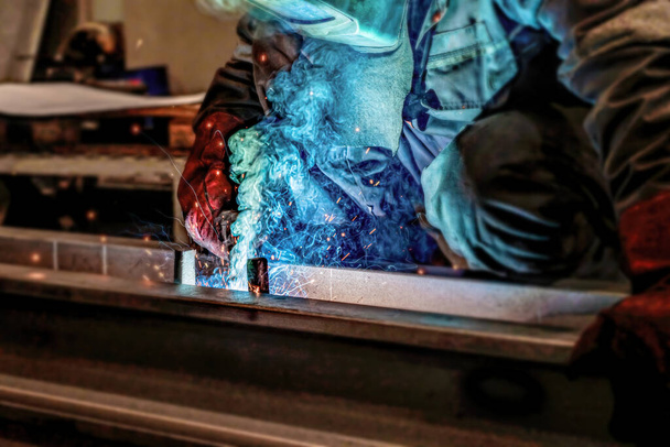 Ένας εργαζόμενος συγκόλλησης μετάλλων εμπλέκεται σε συγκόλληση σε ένα εργαστήριο. - Φωτογραφία, εικόνα
