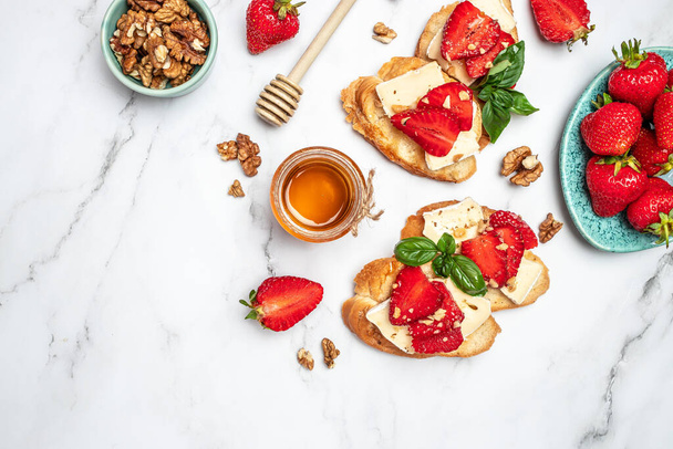 Two toasts or bruschetta with trawberries, cheese camembert nuts and honey. Summer breakfast. Healthy, clean eating. Vegan or gluten free diet. - Photo, Image