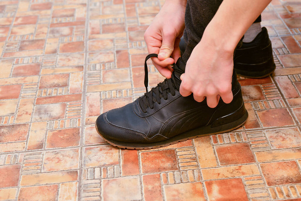 Egy férfi cipőt vesz fel és beköti a cipőfűzőjét otthon a folyosón.. - Fotó, kép