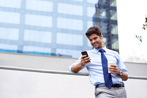 A well-deserved break. A low angle shot of a handsome young businessman using his cellphone in the city - Foto, Imagen