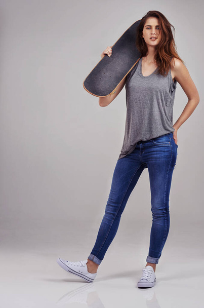 Το σκέιτμπορντ δεν είναι χόμπι, είναι τρόπος ζωής. Full length studio πορτρέτο της άνετα ντυμένος νεαρή γυναίκα που κατέχουν σε ένα skateboard - Φωτογραφία, εικόνα