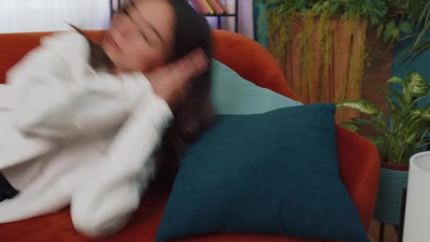 Tired caucasian adult girl lying down in bed taking a rest at home. Carefree young woman napping, falling asleep on comfortable orange sofa with pillows. Closed her eyes enjoy daytime nap alone - Metraje, vídeo