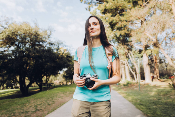 Joven turista viajera, vistiendo camiseta turquesa y una mochila, tomando fotos mientras camina por el parque. Foto de alta calidad - Foto, Imagen