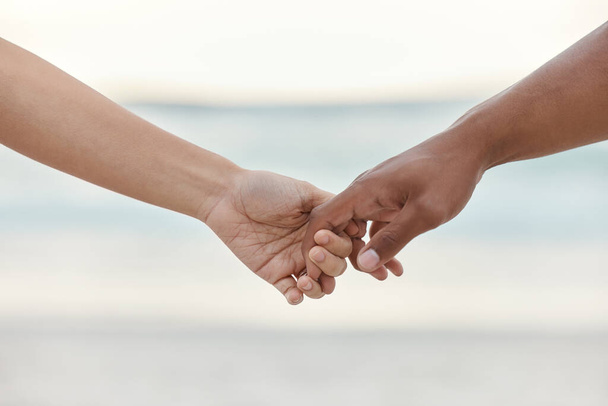 Touch, love and support with interracial couple holding hands in a committed, loving and close relationship. Closeup hands of man and woman enjoying beach travel, sea vacation or holiday and romance. - Photo, Image