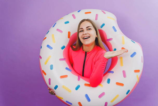 Attractive emotional woman in stylish pink swimsuit with donut inflatable ring on plain background. Beach fashion - Photo, Image