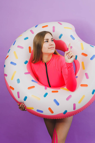 Attractive emotional woman in stylish pink swimsuit with donut inflatable ring on plain background. Beach fashion - 写真・画像