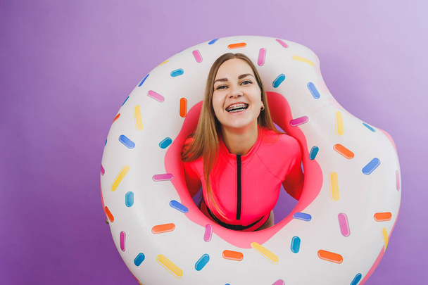 Attractive emotional woman in stylish pink swimsuit with donut inflatable ring on plain background. Beach fashion - Photo, Image