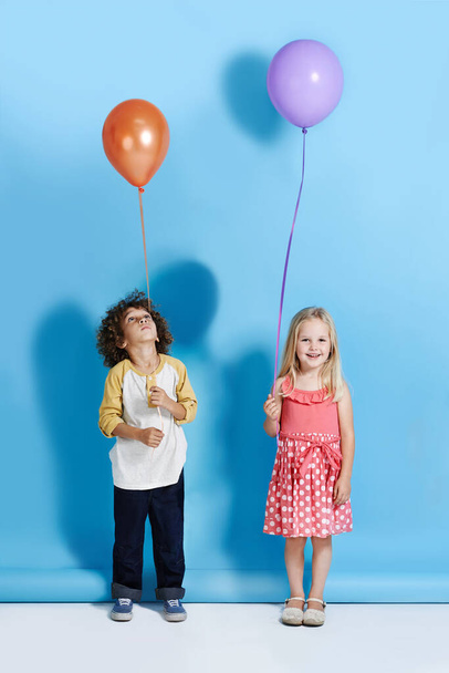 Why wont mine go as high as hers. A cute little girl and boy standing in a studio holding a balloon - Foto, afbeelding