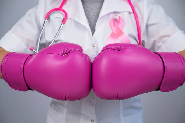 Faceless female doctor in pink boxing gloves with a pink ribbon on a gray background. Fight against breast cancer - Fotó, kép