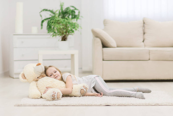Photo of little girl laying on the floor with teddy bear. Concept of small blond girl. - Fotoğraf, Görsel