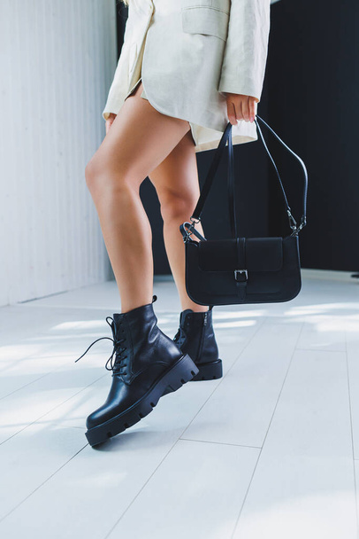 Fashionable leather boots on a woman's leg, close-up, fashionable. Leather bag in female hands. - Фото, зображення