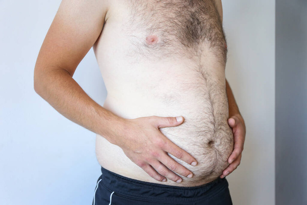 a man holds a big belly against a white wall. Obesity, beer belly - Foto, afbeelding