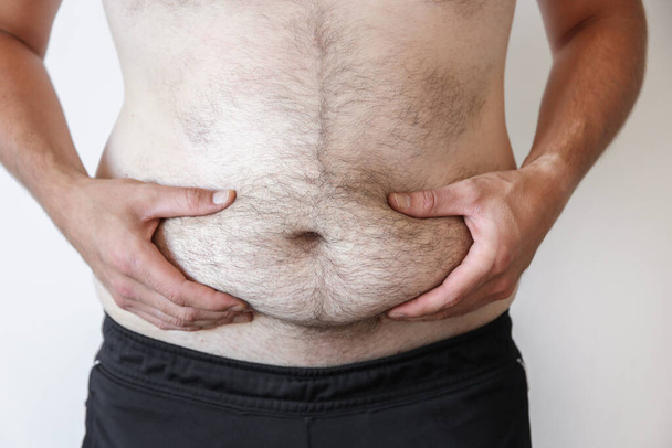 a man holds a big belly against a white wall. Obesity, beer belly - Foto, Bild