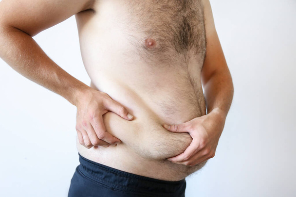 a man holds a big belly against a white wall. Obesity, beer belly - Photo, Image