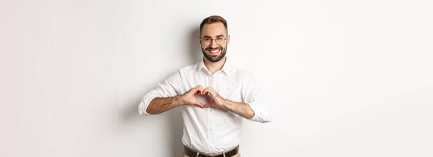 Handsome manage showing heart sign and smiling, I love you gesture, standing over white background. - Foto, Imagem