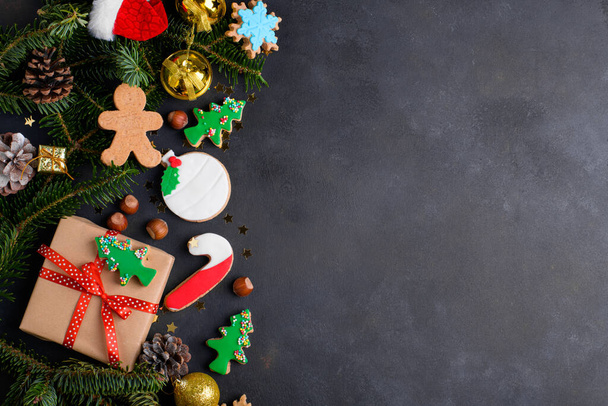 Christmas cookies background. Christmas gingerbread cookies with sugar paste and natural fir tree and Christmas decoration on dark background. Christmas background, top view, flat lay, copy space - Photo, Image