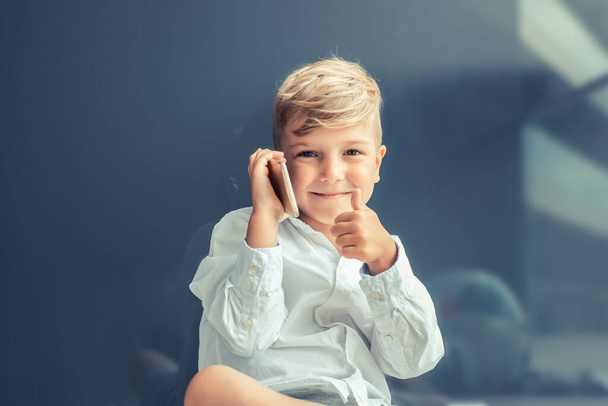 Happy boy showing thumbs up while talking on mobile phone and looking at camera. - Fotoğraf, Görsel