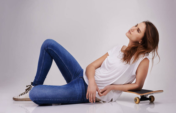 Dreaming of that half pipe. Studio portrait of an attractive young woman lying on the floor with a skateboard - Fotó, kép