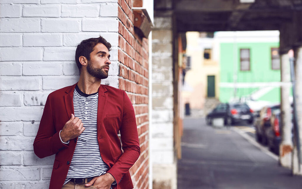 After some time you become part of the city. a handsome young man leaning against a wall outside in the city with one hand touching his jacket - Foto, Imagen