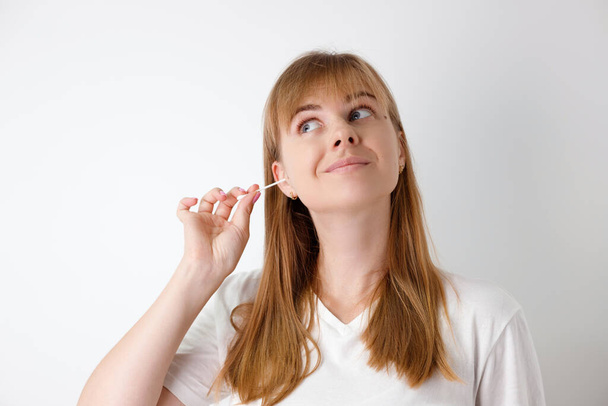 Retrato de uma jovem bela mulher caucasiana cuidadosamente limpando as orelhas com um cotonete. O conceito de higiene e cuidados de saúde. - Foto, Imagem