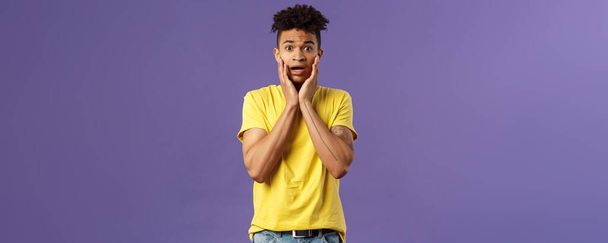 Oh no what do. Portrait of worried, anxious panicking young man feel concerned and confused, hold face and gasping anxious, staring camera alarmed, standing purple background. - Foto, Imagem