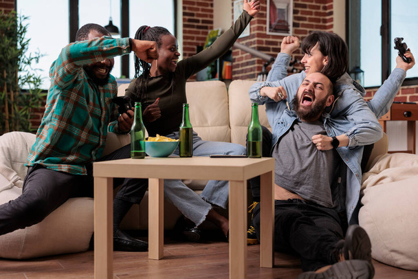 Různorodá skupina lidí, kteří oslavují videohry, vyhrává na shromáždění, společně se baví a těší se z vítězství v soutěži. Cítit radost z vítězství hru hrát na televizní konzoli. - Fotografie, Obrázek