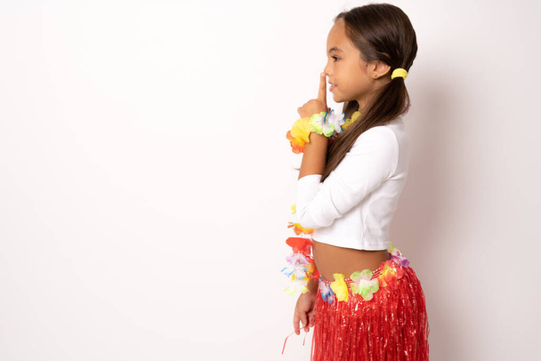 vista lateral da menina criança em pé traje havaiano fazendo silêncio gesto isolado fundo branco - Foto, Imagem