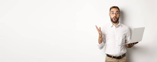 Business. Man holding laptop and looking amazed, surprised with website, standing over white background. Copy space - Foto, immagini