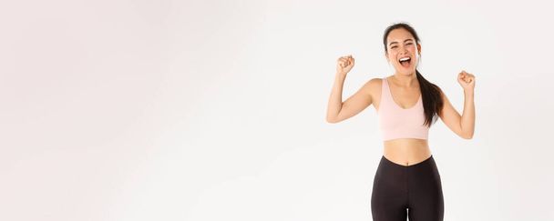 Sport, wellbeing and active lifestyle concept. Empowered and strong asian female athlete, fitness girl encourage herself for good workout, fist pump and shouting supportive, gaining goal. - Photo, Image