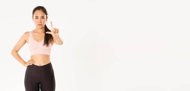 Sport, pohoda a aktivní životní styl koncepce. Vážná nespokojenost asijské žena fitness instruktorka, sportovkyně třesoucí prstem v nesouhlasu, varování nebo nesouhlas, stojící bílé pozadí. - Fotografie, Obrázek
