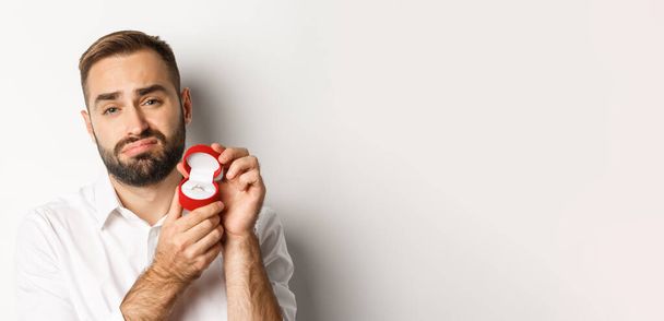 Close-up of hopeful man begging to marry him, looking sad and showing wedding ring, making a proposal, white background. - Foto, Bild
