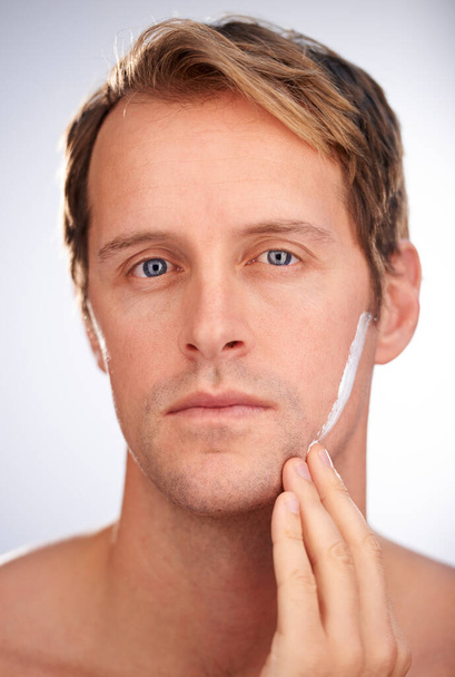 Moisturiser, the modern mans warpaint. Portrait of a handsome man focusing on applying moisturiser - Photo, Image