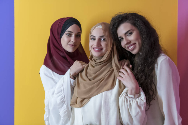 Group portrait of beautiful Muslim women two of them in a fashionable dress with hijab isolated on a yellow background. High quality photo - Фото, изображение