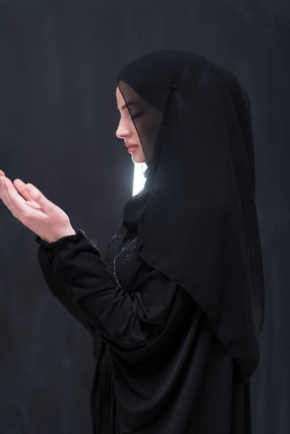 Portrait of beautiful muslim woman in fashionable dress with hijab making traditional prayer to God keeps hands in praying gesture isolated on black background. High quality photo - Valokuva, kuva