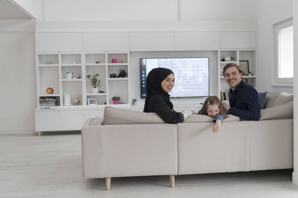 Happy Muslim family with daughter woman in traditional fashionable dress having fun and good time together while sitting on sofa. High quality photo - Valokuva, kuva