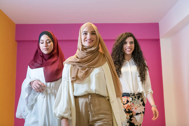 Group portrait of beautiful Muslim women two of them in a fashionable dress with hijab isolated on a pink background. High quality photo - Фото, изображение