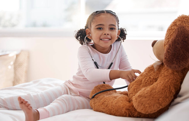 Children, stethoscope and teddy bear with a girl playing doctor in her bedroom at home with a stuffed animal. Imagination, healthcare and medicine with a cute female child being a pretend nurse. - Foto, afbeelding