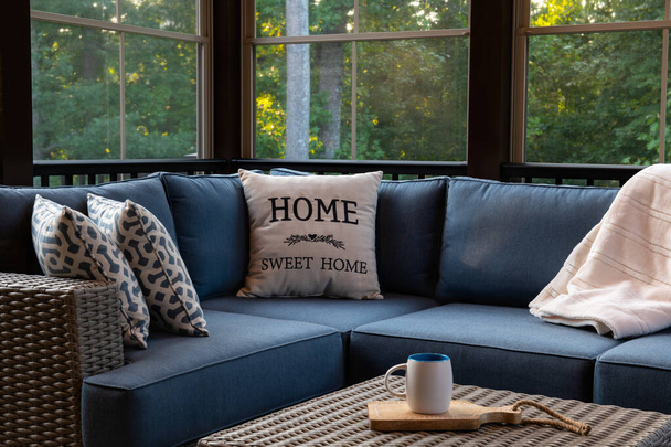 Un acogedor rincón de una sala de estar al aire libre con ventanas de porche modernas, muebles de patio, cojines y almohadas. Bosques en el fondo. - Foto, imagen