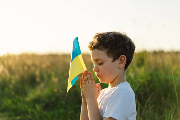Ukraiński chłopiec zamknął jej oczy i modlił się, aby zatrzymać wojnę na Ukrainie na polu o zachodzie słońca. Ręce złożone w koncepcji modlitwy o wiarę, duchowość i religię. Wojna Rosji z Ukrainą. Zatrzymać wojnę. - Zdjęcie, obraz