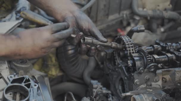 Mechanik holýma a špinavýma rukama utáhne šroub ráčkem do kladky řetězu vačkové hřídele motoru po opravě - Záběry, video