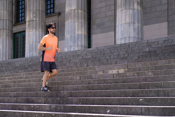 Portrait of handsome attractive mature bearded athletic latin man guy 40s in orange t-shirt running on some stairs - Foto, Bild