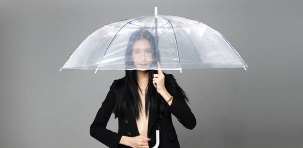 Ασιάτισσα τρανσέξουαλ γυναίκα με μακριά μαύρα ίσια μαλλιά, άνεμος φυσάει ρίξει στον αέρα. Γυναικεία ομπρέλα κατά της ανεμοθύελλας, αίσθηση μόδας αισθησιακό σέξι, γκρι φόντο απομονωμένο αντίγραφο χώρο - Φωτογραφία, εικόνα
