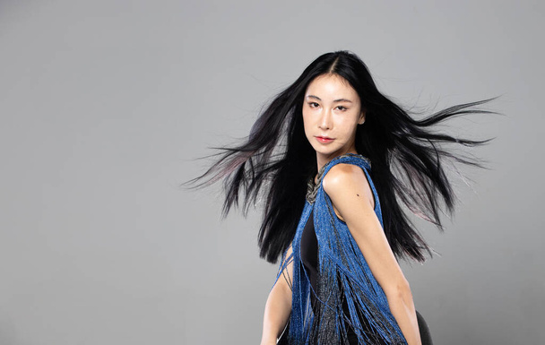 Asijské transgender žena s dlouhými černými rovnými vlasy, vítr foukat do vzduchu. Žena otočit a nosit modré módní smyslné sexy šaty, šedé pozadí izolované kopírovací prostor - Fotografie, Obrázek